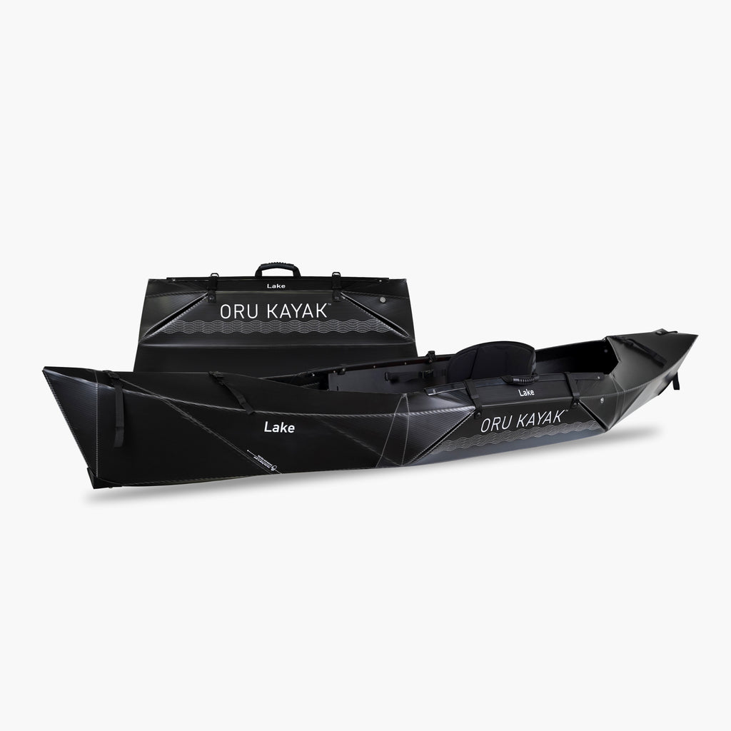 Side view of the Oru Kayak Lake Sport model in black, shown fully assembled in front of its compact folded box form.