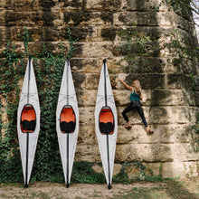 Three bay st kayaks standing against a wall while a woman climbs the wall. 